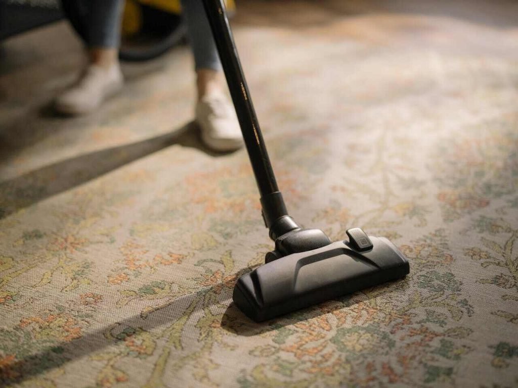 Person cleaning a cozy living room with a vacuum and organized cleaning supplies, showcasing effective deep-cleaning techniques.