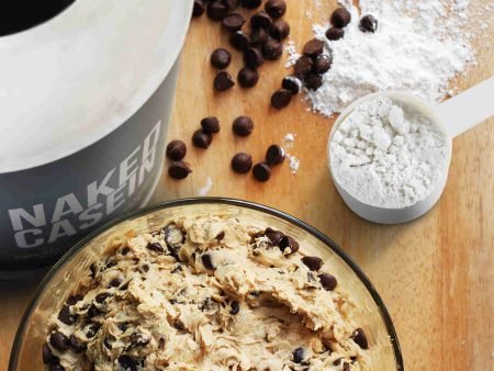Casein protein powder and chocolate chip cookie dough on a wooden surface.